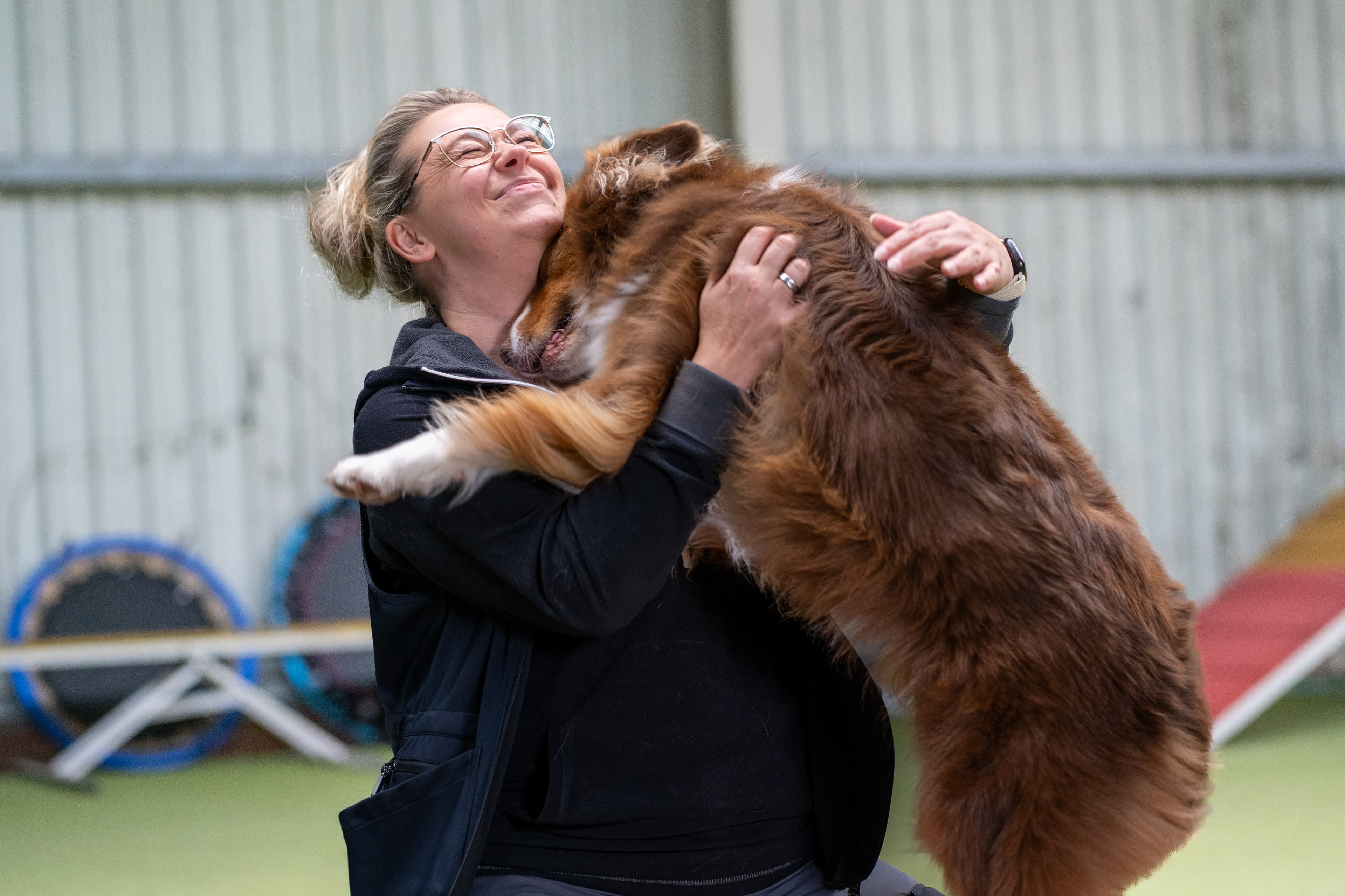 Hundebetreuerin umarmt fröhlich einen großen braunen Hund in der Halle